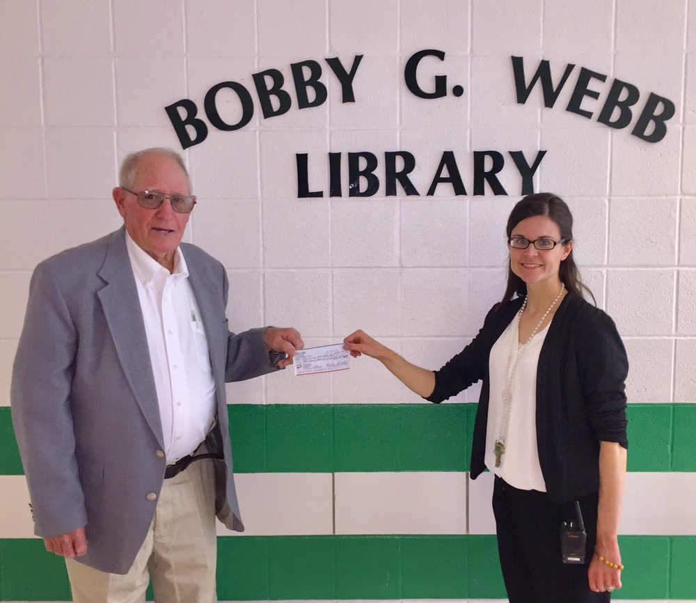 Bobby Webb hands librarian Jessica Uding a check as a donation to the library.
